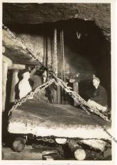 Three workers inside of mine with chained slab of rock