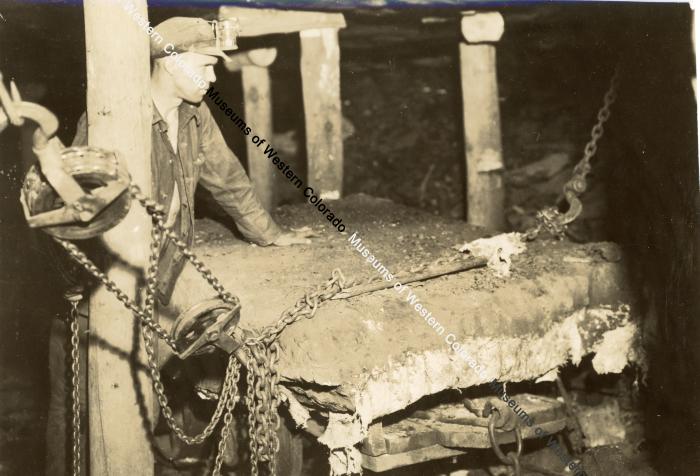 Worker inside of mine with chained slab of rock