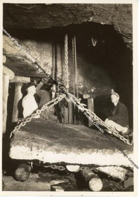 Three workers inside of mine with chained slab of rock